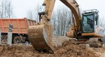 Photograph of an excavator loads a truck with construction sand. High quality photo